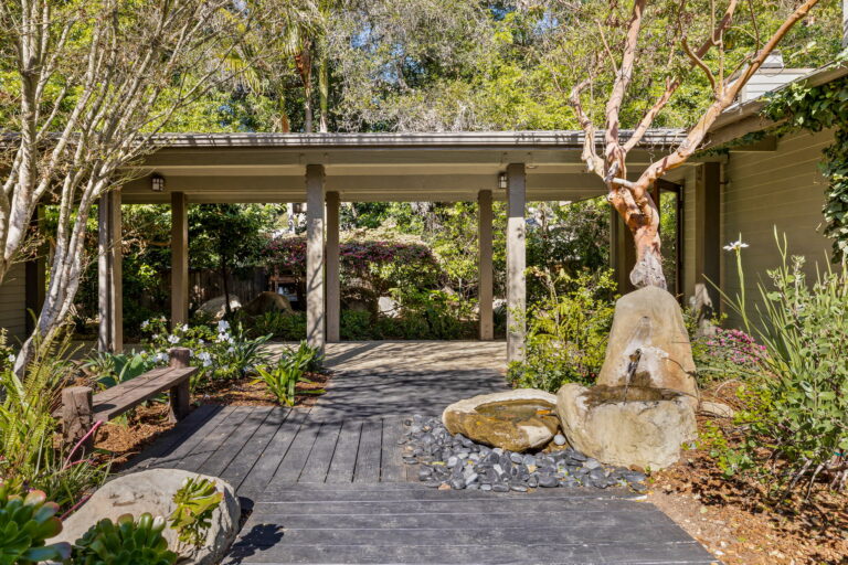 A wooden walkway leads to a large backyard with trees and plants.