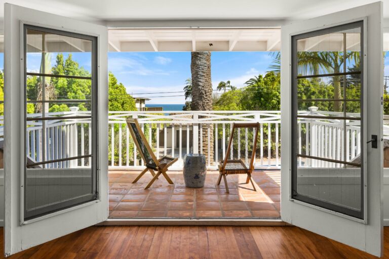 An open door to a balcony overlooking the ocean.