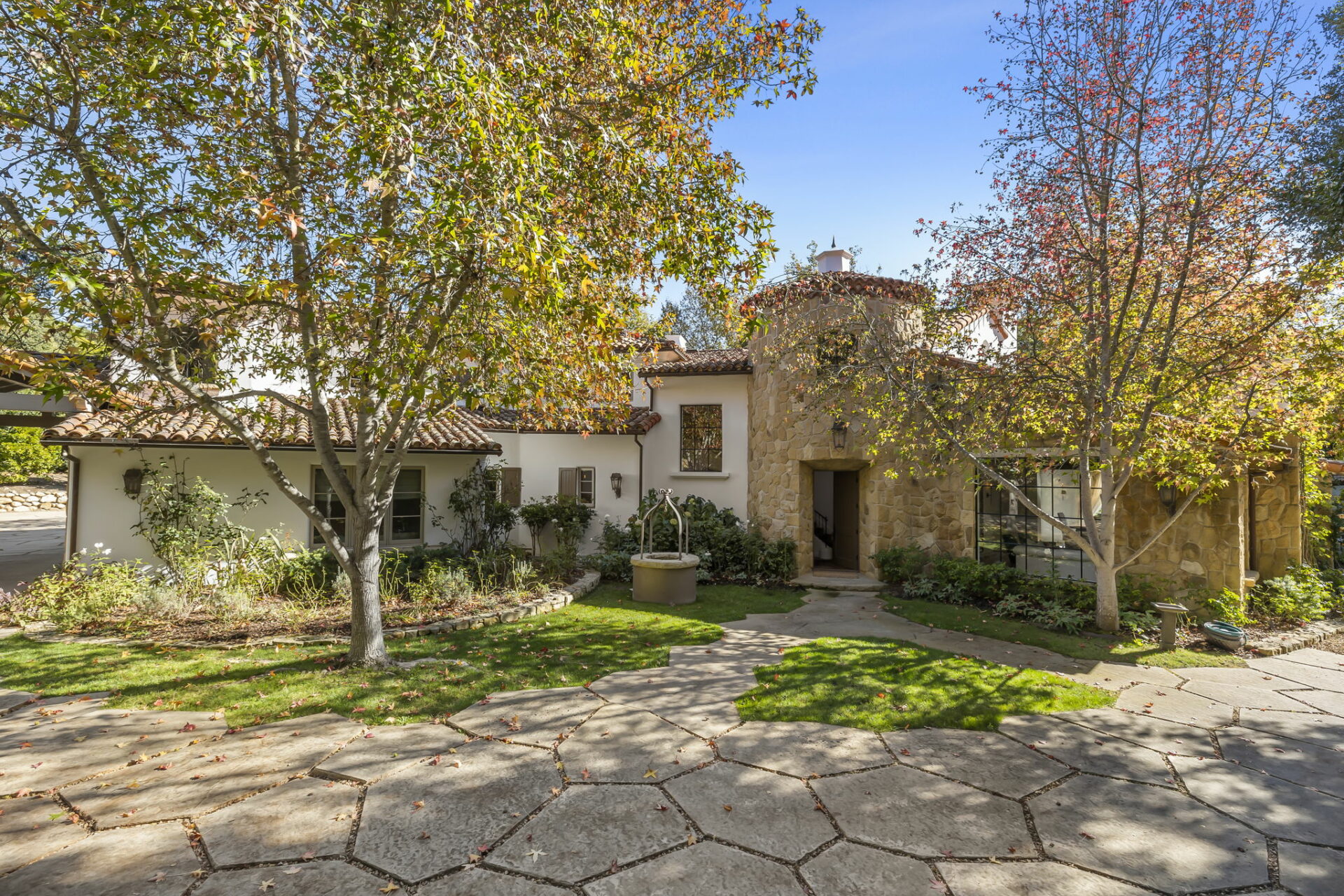 A mediterranean-style house with a stone driveway and surrounding autumn foliage.