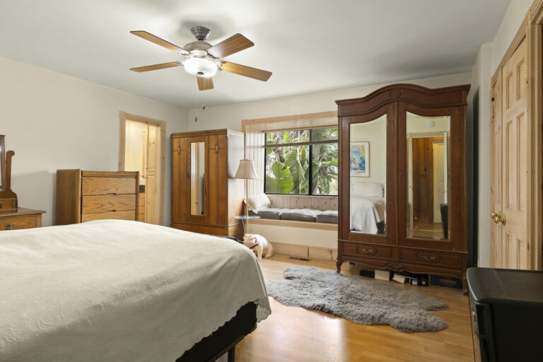 A bedroom with a bed, dresser, mirror, and a fan.