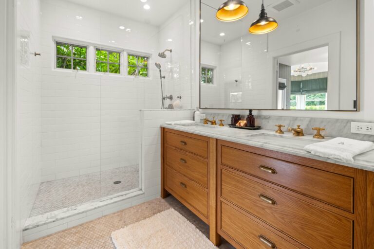 A white bathroom with a wooden vanity and a walk in shower.
