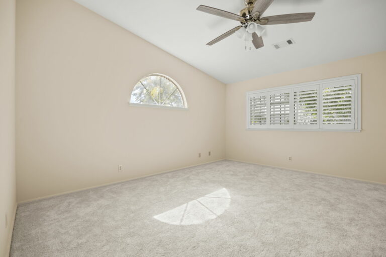 An empty room with a ceiling fan and a window.