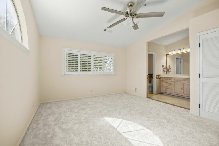 A bedroom with a ceiling fan and white carpet.